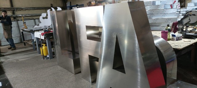 Fabricación de letras volumétricas corpóreas de acero inoxidable en taller para letreros comerciales personalizados.